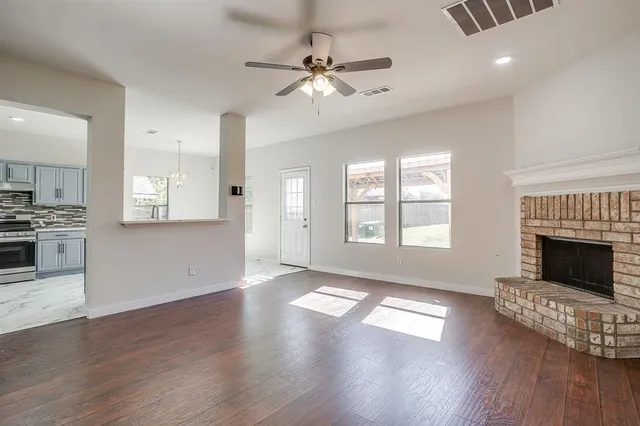 a view of an empty room with wooden floor fireplace and a window