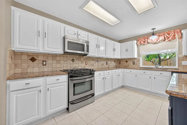 a kitchen with granite countertop white cabinets stainless steel appliances and a window