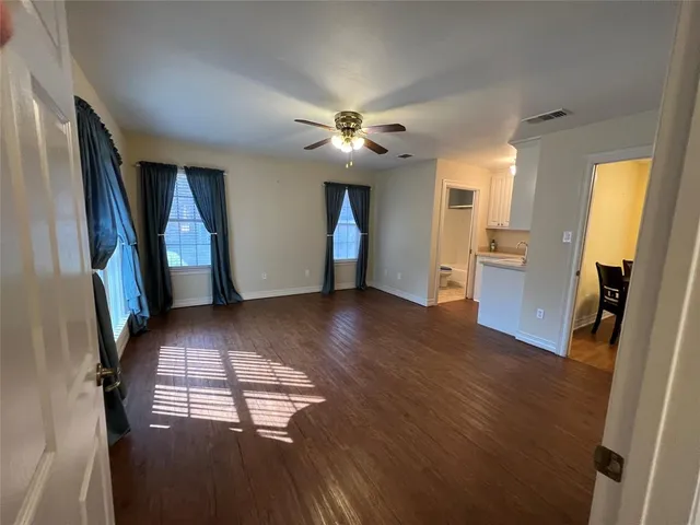 a view of an empty room with chandelier fan and wooden floor