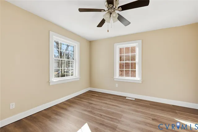 an empty room with wooden floor chandelier fan and windows
