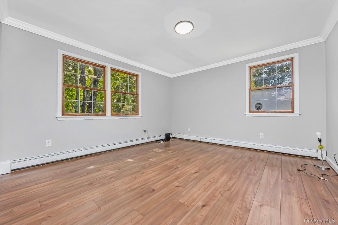 9 Half Moon Pond Road Ridge, NY 11961 - Photo 17 of 26 Wood-finish flooring, light gray wall paint, white crown molding, and two windows with wood trim