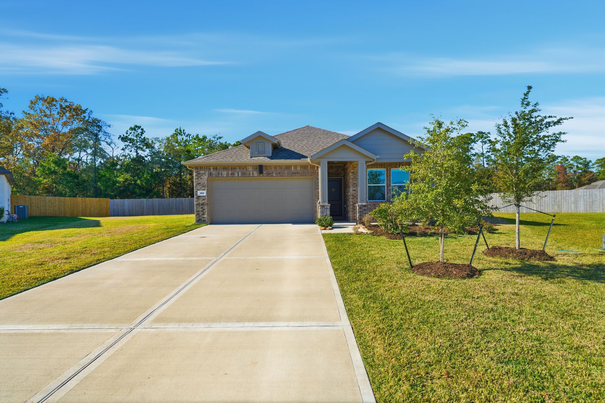 302 Alder Loop Anahuac, TX 77514 - Photo 2 of 34 Spacious driveway leading to a two-car garage. The front yard is well-maintained with small trees and a neat lawn, providing a welcoming curb appeal.