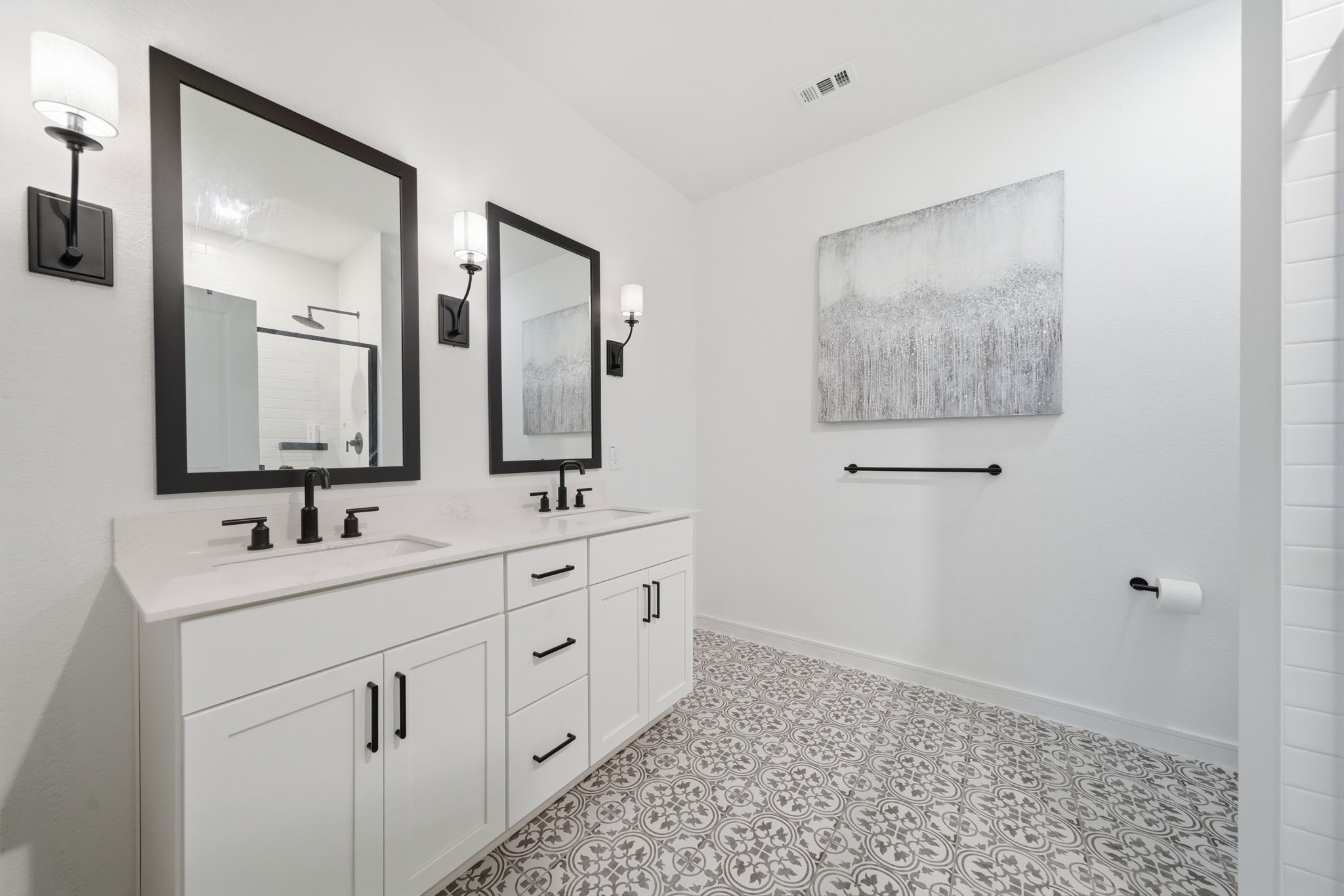 302 Alder Loop Anahuac, TX 77514 - Photo 24 of 34 This Primary Ensuite features a modern design with a double vanity, sleek black fixtures, and elegant patterned floor tiles. The bright space is enhanced by large mirrors, stylish wall sconces, creating a clean and contemporary look.