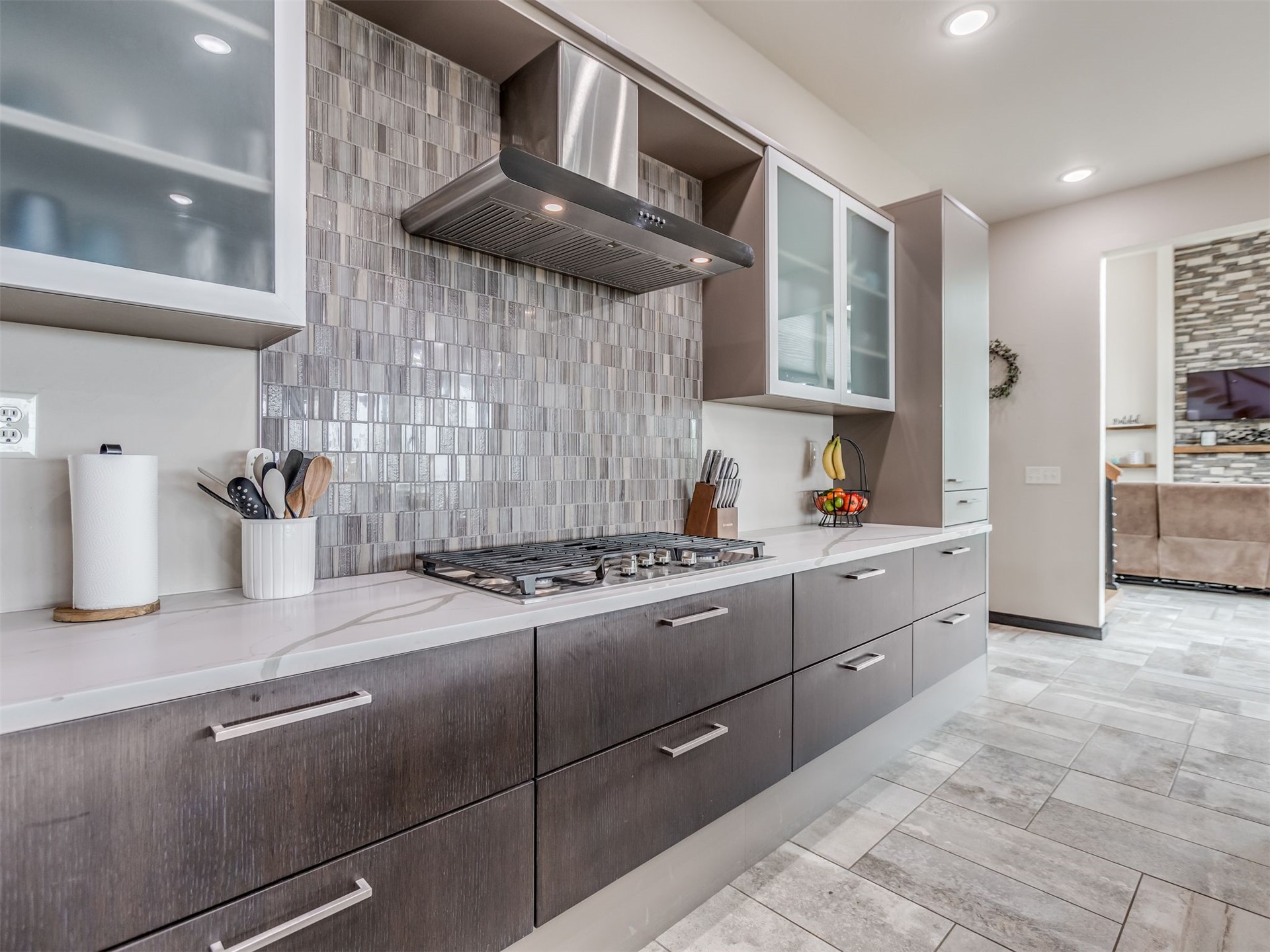 1073 Hidden Ridge Road Stigler, OK 74462 - Photo 18 of 56 Contemporary kitchen featuring dark wood-finish cabinetry, light-toned countertops, a full-height tiled backsplash, stainless steel range hood, and integrated gas cooktop