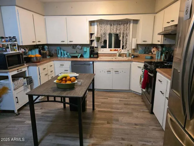 a kitchen with stainless steel appliances granite countertop a stove top oven a sink a refrigerator white cabinets and wooden floor