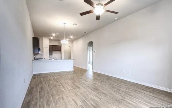 an empty room with wooden floor chandelier fan and windows