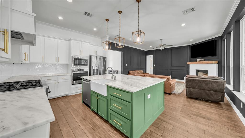 115 Post Oak Way Weatherford, TX 76087 - Photo 38 of 39 Dual tone kitchen featuring crown molding, open floor plan, an island with sink, a fireplace, and a ceiling fan