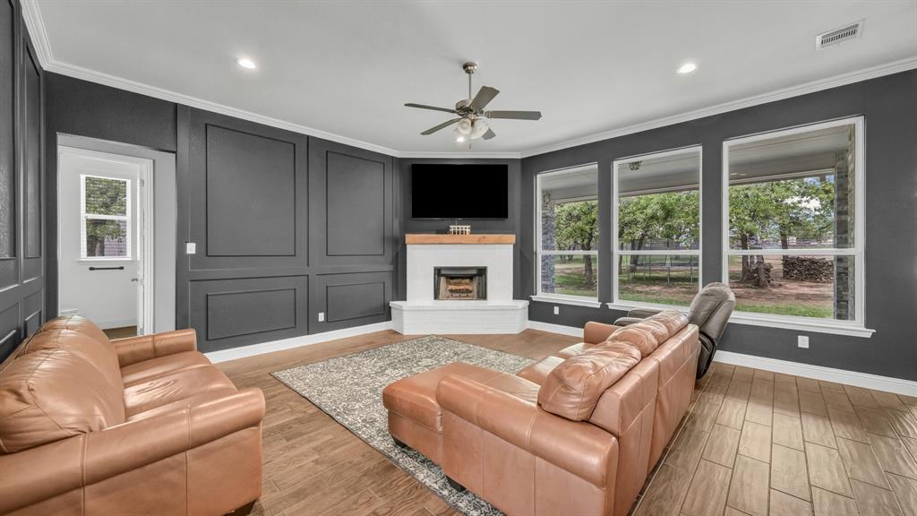 115 Post Oak Way Weatherford, TX 76087 - Photo 7 of 39 Living room featuring wood finish floors, a ceiling fan, a fireplace with raised hearth, recessed lighting, and ornamental molding