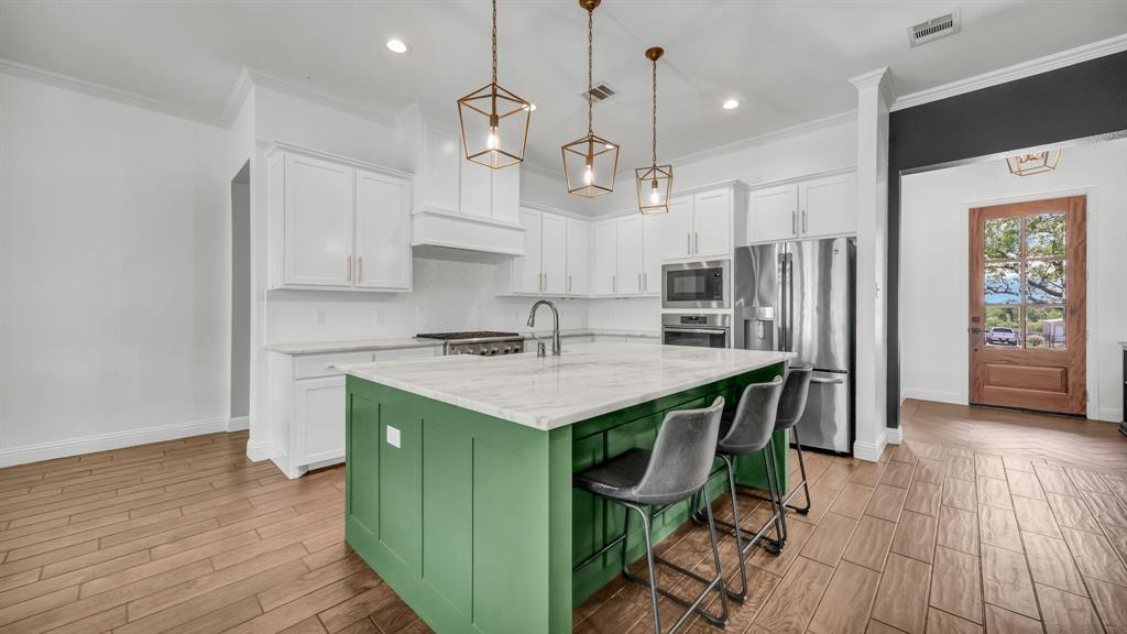 115 Post Oak Way Weatherford, TX 76087 - Photo 10 of 39 Two tone kitchen with wood finish floors, stainless steel appliances, a center island with sink, light stone countertops, and dual tone cabinets
