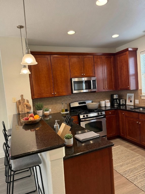1601 Miriam Avenue, Unit 210 Austin, TX 78702 - Photo 6 of 15 Kitchen featuring a breakfast bar, dark stone counters, stainless steel appliances, light wood finished floors, and recessed lighting
