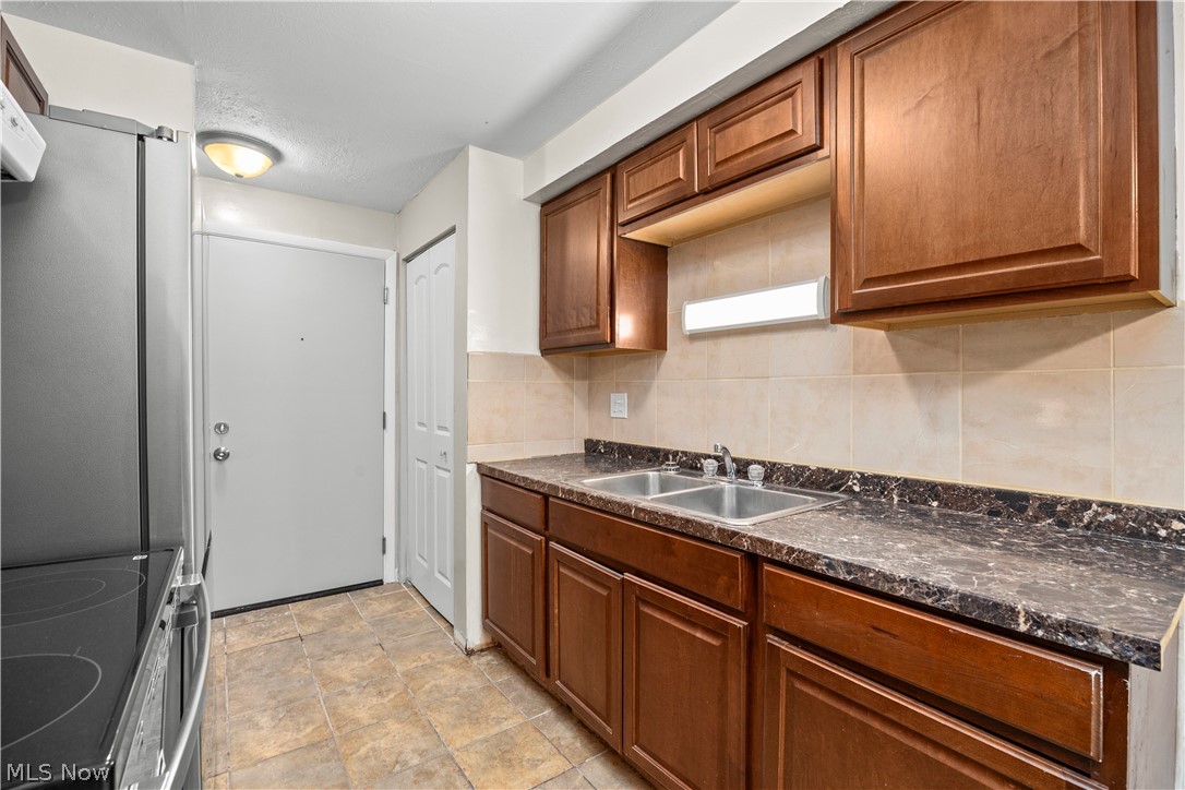 5382 Lee Road, Unit 102 Maple Heights, OH 44137 - Photo 13 of 25 Kitchen with dark countertops, stainless steel appliances, wood finish cabinetry, stone finish floors, and tasteful backsplash