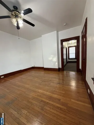 an empty room with wooden floor chandelier fan and windows