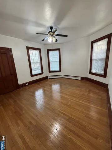 an empty room with wooden floor chandelier fan and windows
