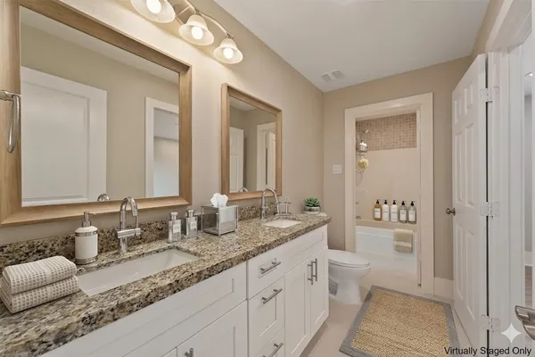a bathroom with double vanity sinks a toilet a mirror and a bathtub