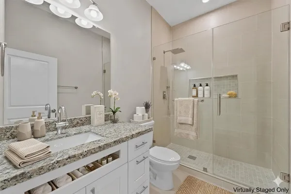 a bathroom with a granite countertop sink a toilet a mirror and shower