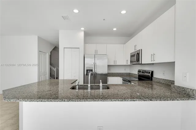 a kitchen with kitchen island granite countertop a sink and a refrigerator
