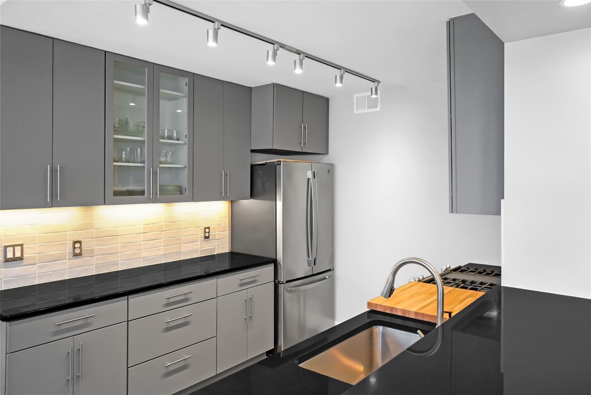 1212 Guadalupe Street, Unit 1004 Austin, TX 78701 - Photo 14 of 33 Kitchen with gray cabinets, glass insert cabinets, tasteful backsplash, rail lighting, and modern cabinets