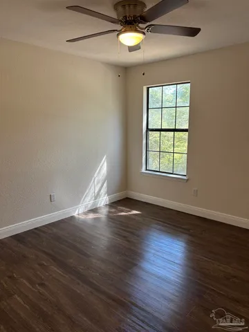 an empty room with wooden floor chandelier fan and windows