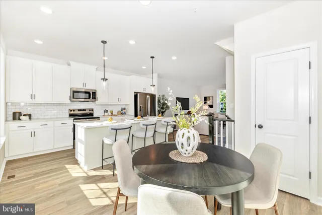 a kitchen with stainless steel appliances kitchen island granite countertop a table chairs and a stove top oven with white cabinets