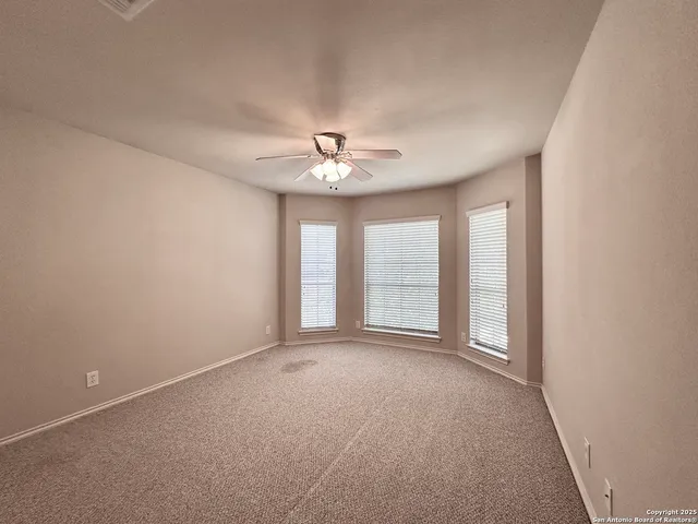 an empty room with chandelier fan and windows
