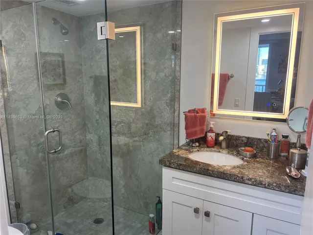 a bathroom with a granite countertop sink a mirror and shower
