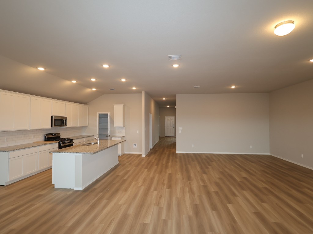 13709 Warnock Trail Manor, TX 78653 - Photo 3 of 25 a large kitchen with kitchen island a stove a sink dishwasher a refrigerator and white cabinets with wooden floor