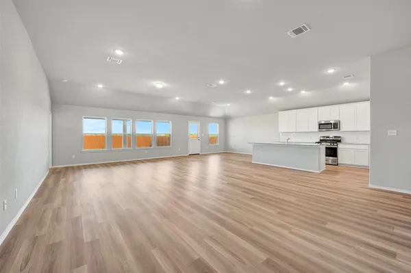 a view of an empty room with wooden floor and a kitchen
