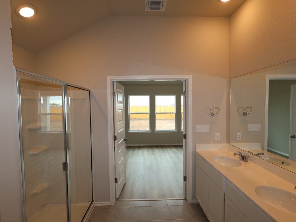 13709 Warnock Trail Manor, TX 78653 - Photo 9 of 25 a en suite bathroom with a double vanity sink a large mirror and a bathtub