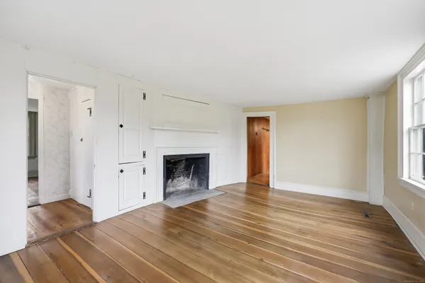 an empty room with wooden floor fireplace and windows