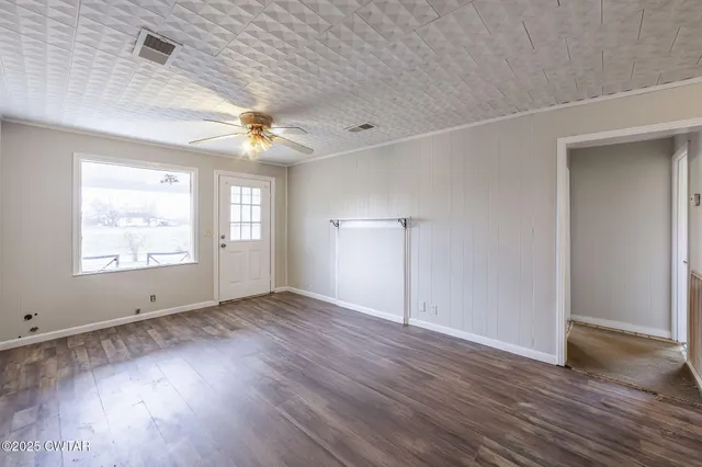 an empty room with wooden floor chandelier fan and windows