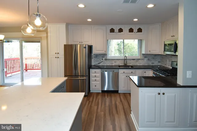 a kitchen with stainless steel appliances granite countertop a refrigerator a sink dishwasher a stove and white countertops with wooden floor