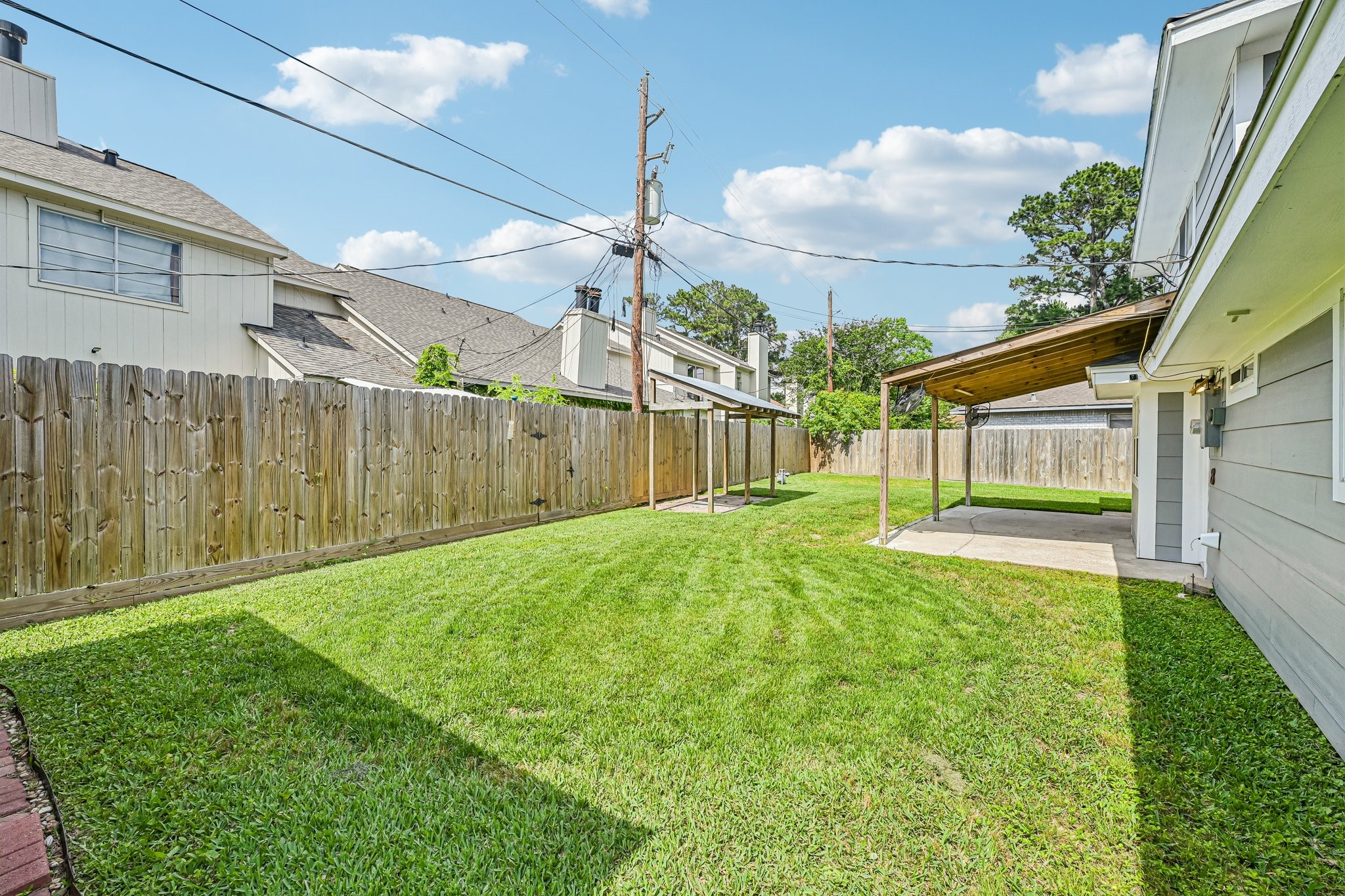 8 Arlington Street Conroe, TX 77301 - Photo 35 of 37 The photo showcases a spacious backyard with well-maintained grass, a wooden privacy fence, and a covered patio area attached to the house, perfect for outdoor activities and relaxation.