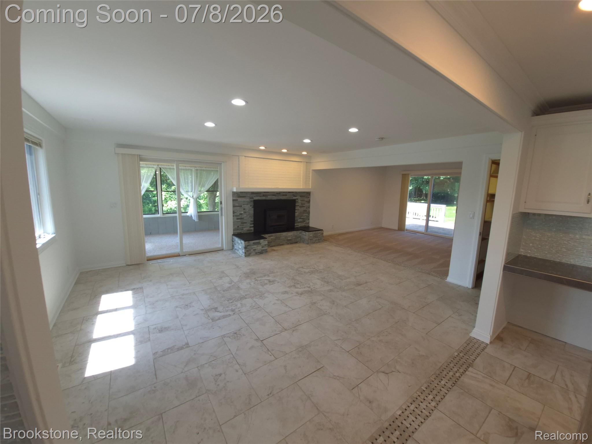 4140 South Henderson Road Davison, MI 48423 - Photo 29 of 98 Spacious open-concept room featuring light-toned tile flooring, a stone-faced fireplace with a mantel, recessed lighting, and sliding glass doors opening to an enclosed patio