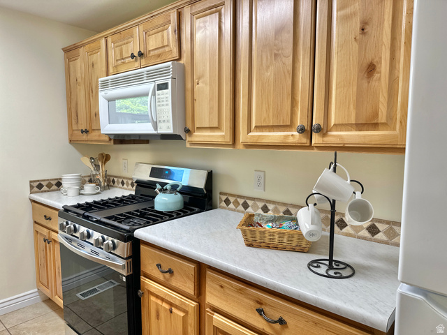 624 East Cutler Springville, UT 84663 - Photo 8 of 24 Kitchen featuring natural wood cabinetry, light-toned countertops, a multi-tone tile backsplash, Microwave, and a gas range