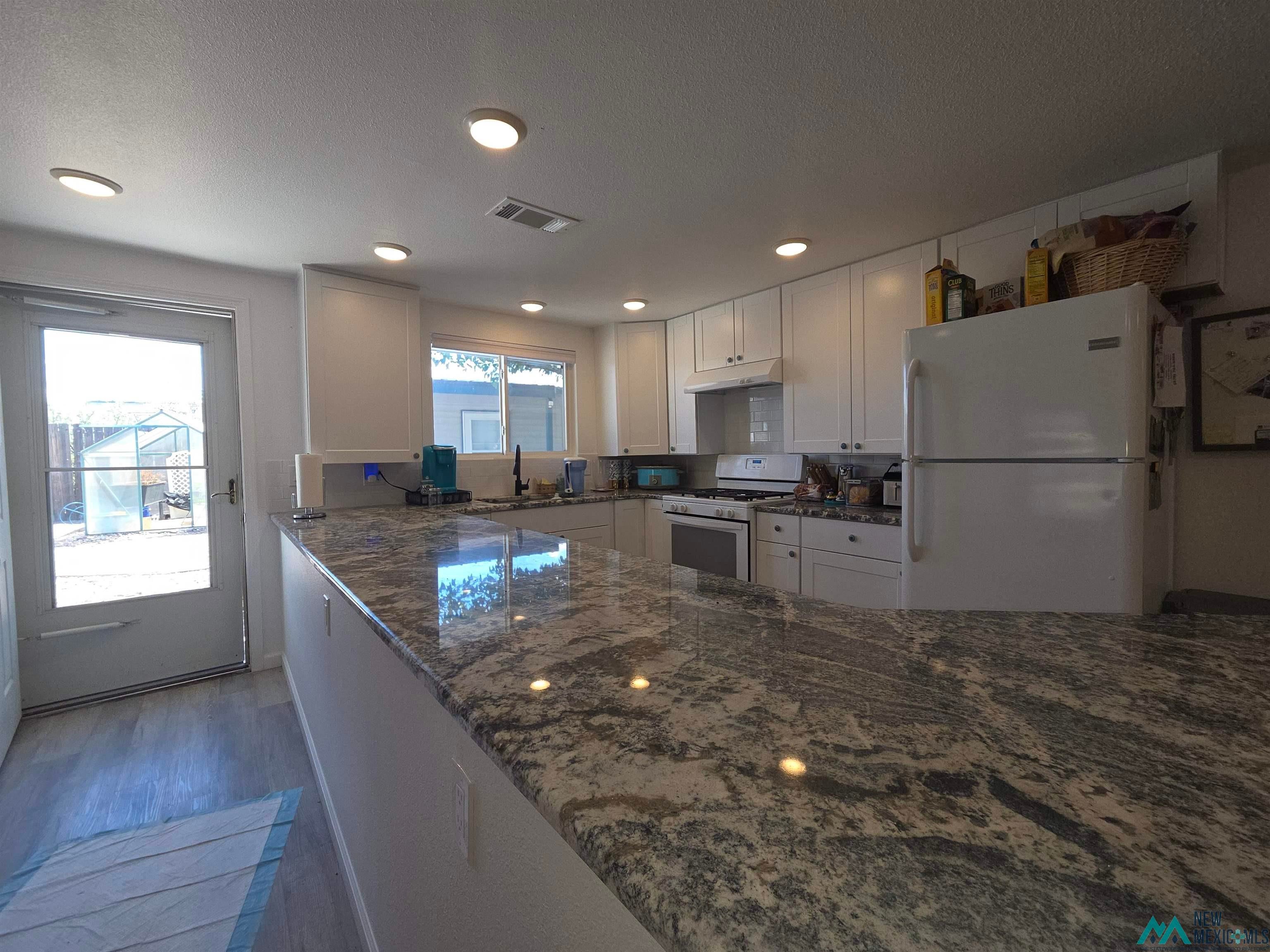 407 Bass Road Elephant Butte, NM 87935 - Photo 25 of 54 Kitchen with dark stone countertops, white appliances, white cabinetry, wood finished floors, and a textured ceiling