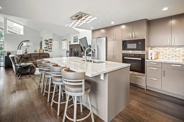 a kitchen with stainless steel appliances granite countertop a stove top oven a refrigerator a dining table and chairs with wooden floor