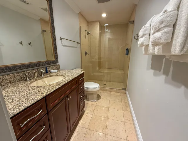 a bathroom with a granite countertop sink a toilet a mirror and shower