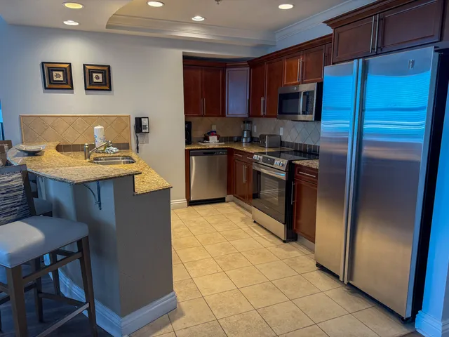 a kitchen with stainless steel appliances granite countertop a refrigerator a sink a stove a dining table and chairs