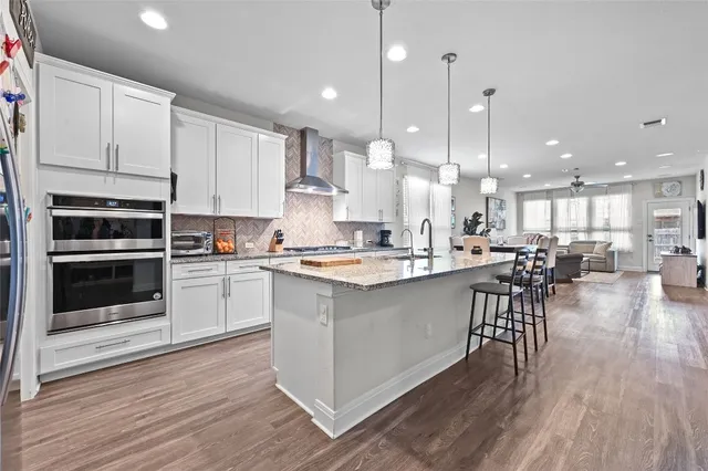 a kitchen with stainless steel appliances kitchen island granite countertop a stove a sink a refrigerator and white cabinets with wooden floor