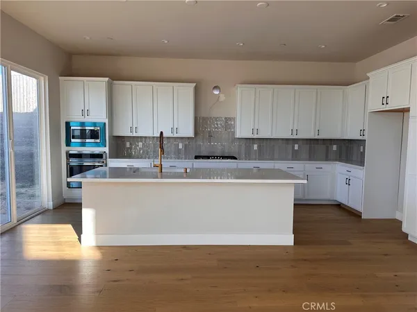 a large white kitchen with stainless steel appliances granite countertop a stove a sink a refrigerator and white cabinets with wooden floor