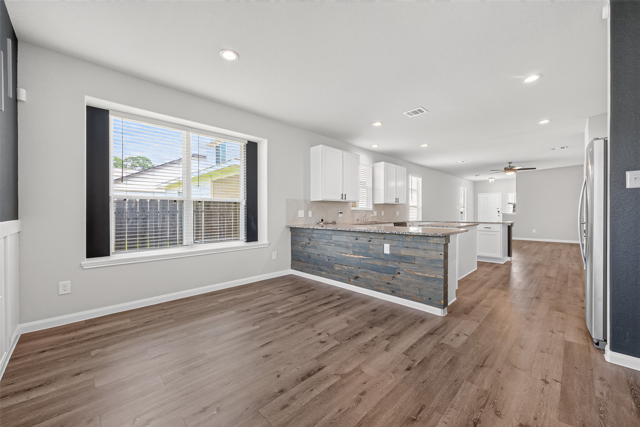 2526 Sturgeon Way Conroe, TX 77384 - Photo 9 of 49 This bright, open-concept space features a modern kitchen with a large island and granite countertops, seamlessly connected to a spacious living area with wood flooring and abundant natural light from large windows.