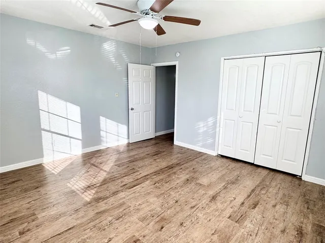 an empty room with wooden floor fan and windows