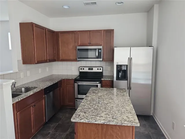 a kitchen with granite countertop wooden cabinets a refrigerator and a stove top oven