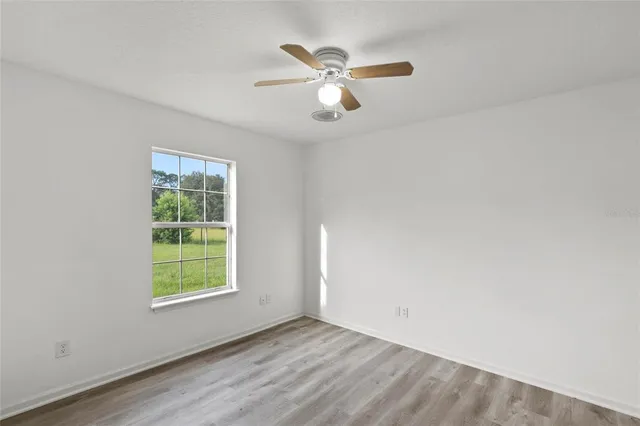 an empty room with wooden floor chandelier fan and windows