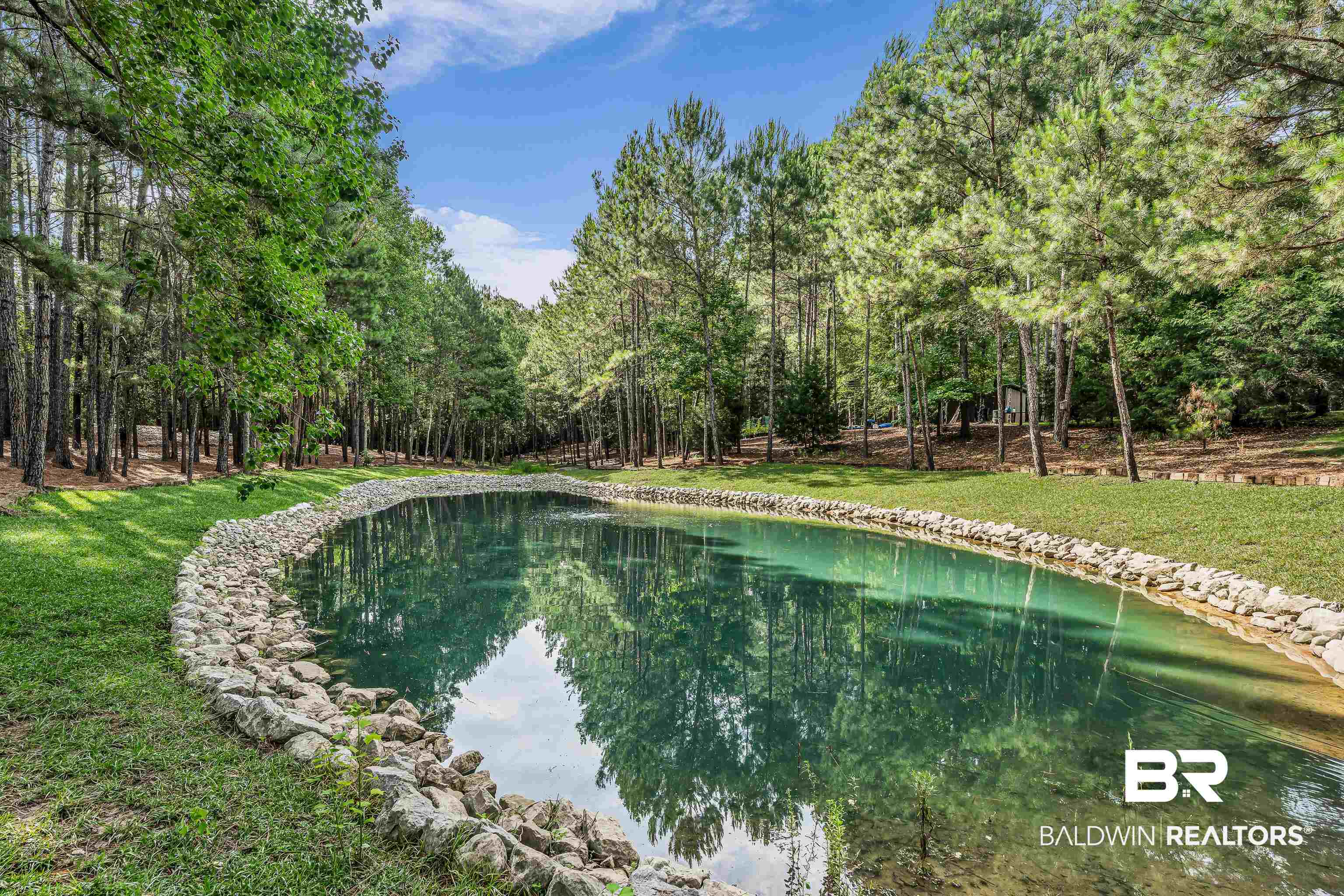 7014 Blakeley Road Daphne, AL 36527 - Photo 10 of 45 Serene pond featuring clear water, a natural rock border, and surrounding green grass