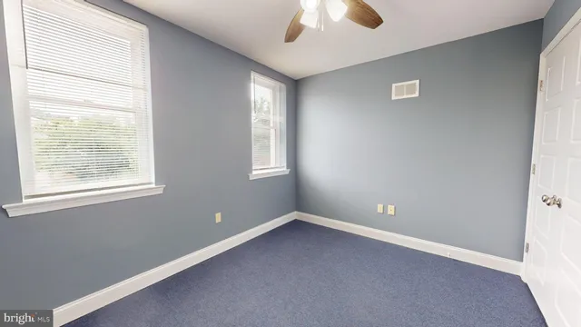 an empty room with chandelier fan and windows
