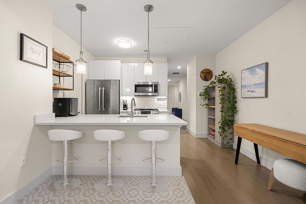 121-127 Portland Street, Unit 307 Boston, MA 02114 - Photo 7 of 27 a kitchen with stainless steel appliances kitchen island granite countertop a refrigerator a stove a dining table and chairs with wooden floor