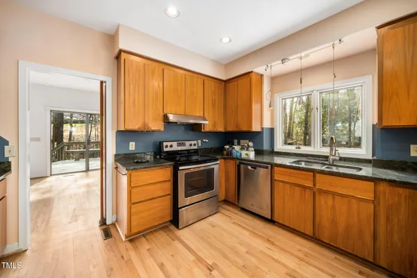 a kitchen with stainless steel appliances kitchen island granite countertop a stove a sink and white cabinets with wooden floor