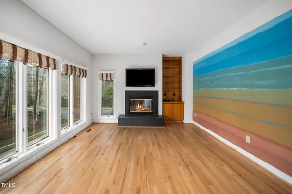 a view of an empty room with wooden floor fireplace and a window