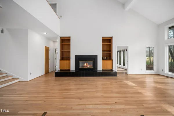 a view of an empty room with wooden floor fireplace and a window